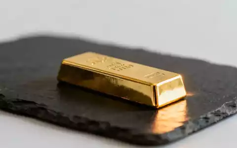Ein glänzender Goldbarren auf einer dunklen Schieferplatte bei gedimmter, professioneller Beleuchtung. - Foto: über boerse-global.de