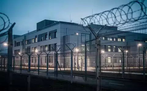 Modernes Gebäude einer forensischen Psychiatrie bei Dämmerung mit Sicherheitszaun und dezenter Beleuchtung. - Foto: über boerse-global.de