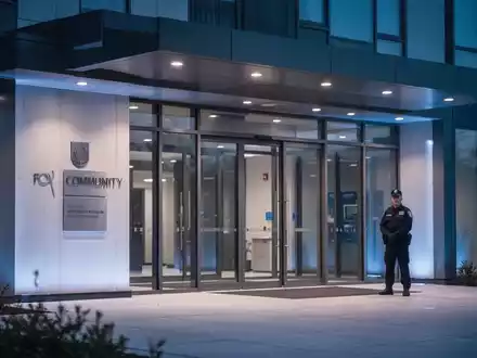 Ein Sicherheitsmitarbeiter bewacht den Eingang eines Gemeindegebäudes in der Abenddämmerung. - Foto: über boerse-global.de