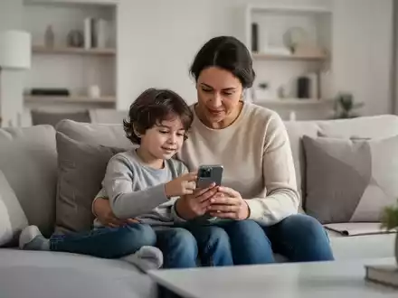 Ein Elternteil und ein Kind schauen gemeinsam auf einen Smartphone-Bildschirm in einem hellen, modernen Wohnzimmer. - Foto: über boerse-global.de