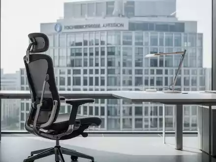 Ein moderner, minimalistischer Büroarbeitsplatz mit einem ergonomischen Bürostuhl vor einer Fensterfront. - Foto: über boerse-global.de