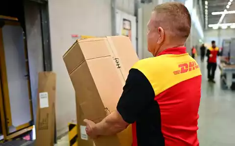 Ein Paketbote schleppt in einem DHL-Standort ein schweres Paket. (Archivbild) - Foto: Sebastian Christoph Gollnow/dpa