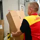 Ein Paketbote schleppt in einem DHL-Standort ein schweres Paket. (Archivbild) - Bild: Sebastian Christoph Gollnow/dpa