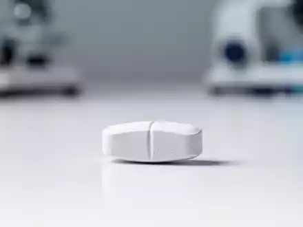 Eine einzelne pharmazeutische Tablette auf einer sauberen, weißen Laboroberfläche als Symbol für moderne Adipositas-Therapie. - Foto: über boerse-global.de