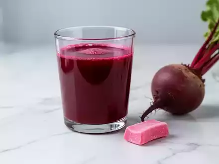 Ein Glas Rote-Bete-Saft steht neben einem Kaugummi auf einem hellen Untergrund als Symbol fĂŒr die Studie zur Blutdrucksenkung. - Foto: ĂŒber boerse-global.de