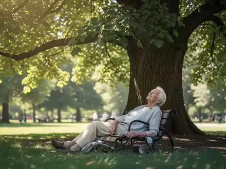 Eine ältere Person ruht sich an einem heißen Sommertag entspannt im schattigen Bereich unter einer großen Baumkrone aus. - Foto: über boerse-global.de