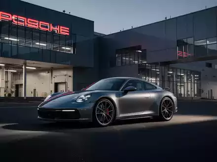 Ein moderner Porsche vor einem Produktionsgebäude bei Dämmerung, symbolisierend die aktuelle Restrukturierung. - Foto: über boerse-global.de