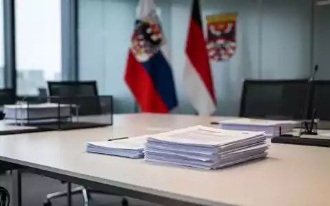 Ein aufgeräumter Schreibtisch mit Dokumenten in einem modernen Regierungsbüro vor einer unscharfen Thüringer Flagge. - Foto: über boerse-global.de