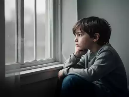 Ein nachdenkliches Kind sitzt allein an einem Fenster, symbolisch für die psychische Belastung junger Menschen. - Foto: über boerse-global.de