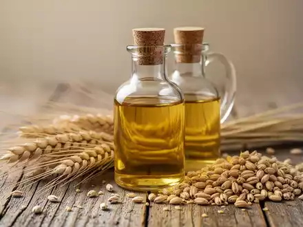 Eine Glasflasche mit Weizenkeimöl neben frischen Weizenähren und Weizenkörnern auf einem Holztisch. - Foto: über boerse-global.de