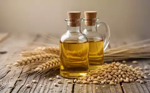 Eine Glasflasche mit Weizenkeimöl neben frischen Weizenähren und Weizenkörnern auf einem Holztisch. - Foto: über boerse-global.de