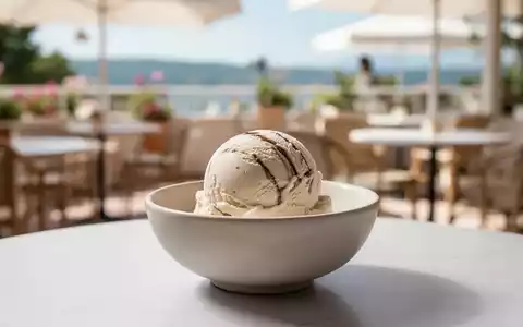 Eine einzelne Kugel Eiscreme in einer minimalistischen Schale vor einem unscharfen Hintergrund einer sommerlichen Terrasse. - Foto: über boerse-global.de