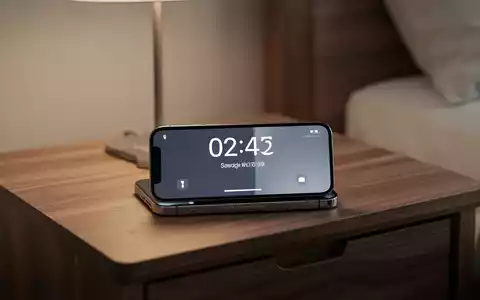Ein iPhone im StandBy-Modus zeigt eine digitale Uhr auf einem Nachttisch bei sanfter Beleuchtung. - Foto: über boerse-global.de