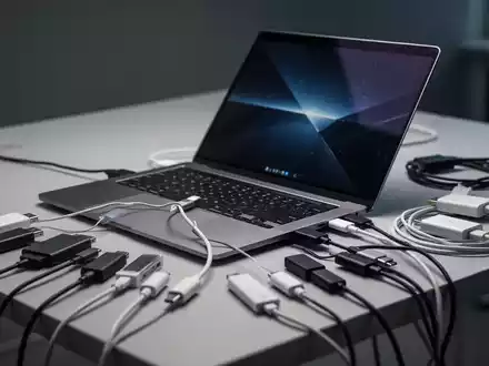 Ein flacher moderner Laptop auf einem Schreibtisch, umgeben von zahlreichen Adaptern und Kabeln. - Foto: über boerse-global.de