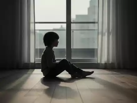 Ein einsames Kind sitzt nachdenklich im gedimmten Licht eines Zimmers und reflektiert die psychische Belastung. - Foto: über boerse-global.de