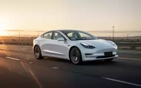 Weißer Tesla Model 3 auf einer Autobahn bei malerischem Sonnenuntergang, der Meilensteine des autonomen Fahrens symbolisiert. - Foto: über boerse-global.de