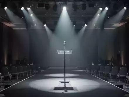 Ein leeres Rednerpult mit Mikrofon auf einer Bühne unter atmosphärischer Beleuchtung in einem Konferenzsaal. - Foto: über boerse-global.de