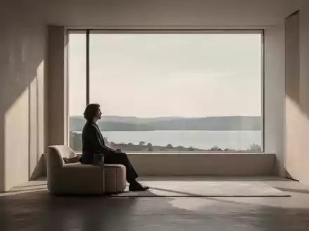 Eine nachdenkliche Person in einem minimalistischen, lichtdurchfluteten Raum blickt aus einem Fenster in eine ruhige Landschaft. - Foto: über boerse-global.de