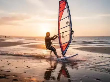 Person beim Windsurfen vor der Nordseeküste bei Sonnenuntergang als Ganzkörper-Workout. - Foto: über boerse-global.de