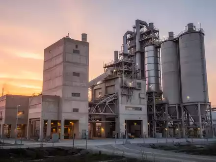 Moderne Zementfabrik bei Sonnenaufgang mit industriellen Silos und Betonstrukturen. - Foto: über boerse-global.de