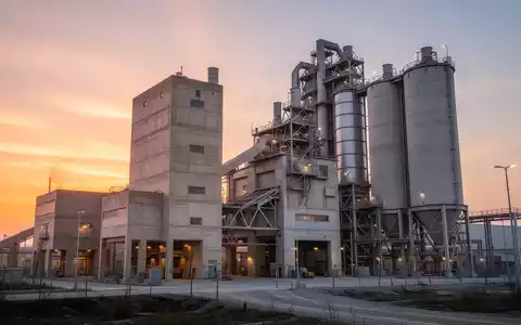 Moderne Zementfabrik bei Sonnenaufgang mit industriellen Silos und Betonstrukturen. - Foto: über boerse-global.de