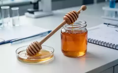 Ein hölzerner Honiglöffel in einem Glas mit rohem Honig auf einem Labortisch, daneben wissenschaftliche Utensilien. - Foto: über boerse-global.de