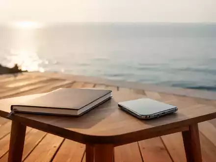Ein geschlossenes Notizbuch und ein umgedrehtes Smartphone auf einem Holztisch vor einer ruhigen Meereskulisse. - Foto: über boerse-global.de