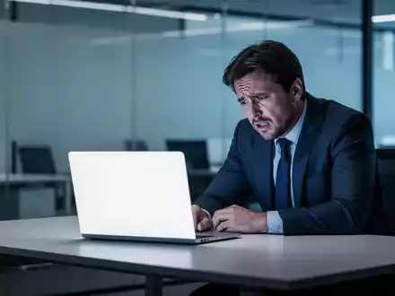 Erschöpfter Büroangestellter vor einem Laptop an einem modernen Schreibtisch, der seine Überforderung mit KI-Technologien ausdrückt. - Foto: über boerse-global.de