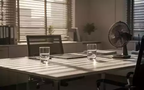 Modernes Büro bei hohen Temperaturen mit Jalousien, einem Ventilator und einem Glas Wasser auf dem Schreibtisch. - Foto: über boerse-global.de