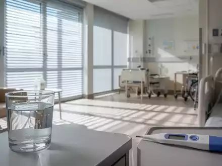 Ein lichtdurchflutetes Seniorenzimmer mit geschlossenen Jalousien zum Hitzeschutz, ein Glas Wasser und ein Thermometer. - Foto: über boerse-global.de