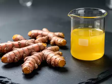 Frische Kurkuma-Wurzeln neben einem Glasgefäß mit gelbem Curcumin-Extrakt in einer Laborumgebung. - Foto: über boerse-global.de