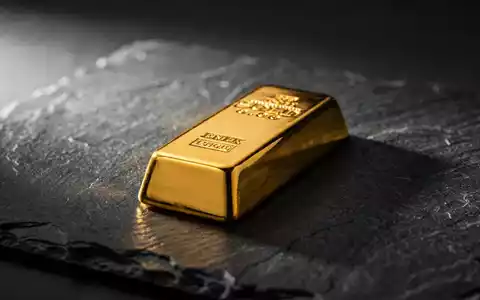 Ein glänzender Goldbarren auf einer dunklen Schieferplatte mit dramatischem Licht. - Foto: über boerse-global.de