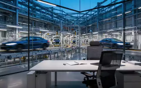 Modernes BMW-Werk bei Dämmerung mit einem leeren, minimalistischen Büroarbeitsplatz im Vordergrund. - Foto: über boerse-global.de