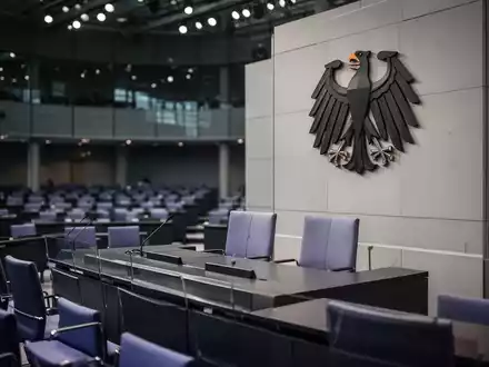 Der Plenarsaal des Deutschen Bundestages mit dem Bundesadler an der Wand bei atmosphärischer Beleuchtung. - Foto: über boerse-global.de