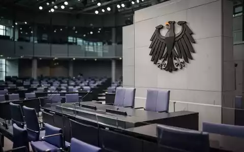 Der Plenarsaal des Deutschen Bundestages mit dem Bundesadler an der Wand bei atmosphärischer Beleuchtung. - Foto: über boerse-global.de