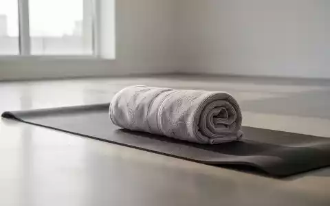 Ein zusammengerolltes Handtuch auf einer Yogamatte in einem hellen, minimalistischen Raum für Fitnessübungen. - Foto: über boerse-global.de