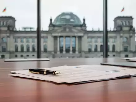 Modernes Büro mit Dokumenten und verschwommenem Parlamentsgebäude im Hintergrund als Symbol für arbeitsrechtliche Reformen. - Foto: über boerse-global.de