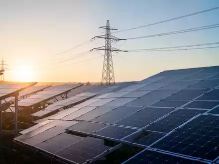 Moderne Solarpark-Anlage mit Strommasten bei Sonnenaufgang als Symbol für die Energiewende und Netzstabilität. - Foto: über boerse-global.de