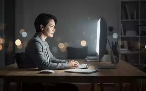 Eine Person sitzt konzentriert vor einem leuchtenden Bildschirm in einem abgedunkelten Büro. - Foto: über boerse-global.de