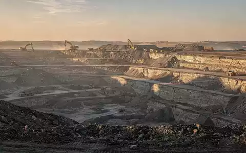 Moderne Tagebau-Mine bei Sonnenaufgang mit schwerem Gerät in einer weiten Landschaft. - Foto: über boerse-global.de