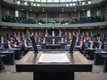 Das Rednerpult im Deutschen Bundestag vor dem unscharfen Plenarsaal bei einer politischen Sitzung. - Foto: über boerse-global.de