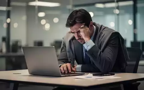 Erschöpfter Büroangestellter am Schreibtisch vor einem Laptop, symbolisiert die negativen Folgen von unbezahlter Mehrarbeit. - Foto: über boerse-global.de