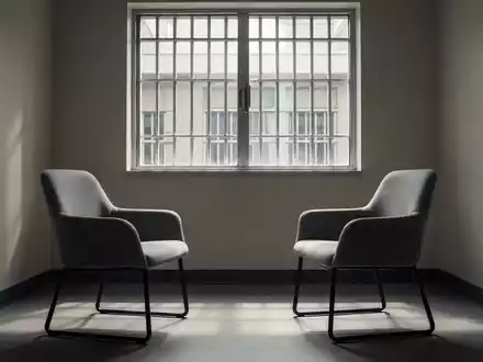 Ein heller, minimalistischer Besprechungsraum in einer Justizvollzugsanstalt mit zwei gegenüberstehenden Stühlen. - Foto: über boerse-global.de