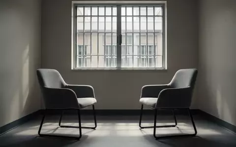 Ein heller, minimalistischer Besprechungsraum in einer Justizvollzugsanstalt mit zwei gegenüberstehenden Stühlen. - Foto: über boerse-global.de