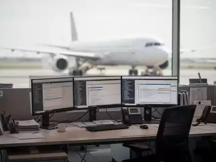 Blick aus einem Büro auf das Flughafengelände mit einem Flugzeug vor einem modernen Terminal. - Foto: über boerse-global.de