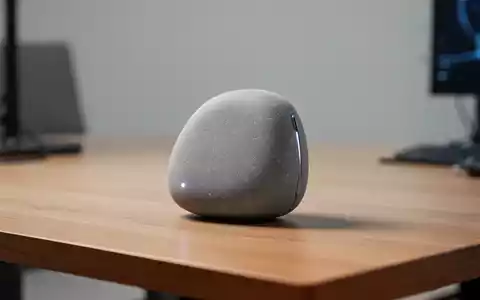 Ein minimalistisches, taschengroßes KI-Hardwaregerät auf einem Holztisch in einer modernen, professionellen Umgebung. - Foto: über boerse-global.de