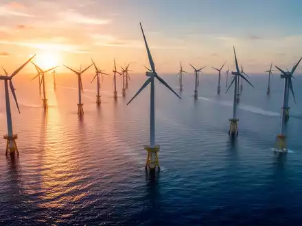Mehrere große Offshore-Windkraftanlagen im Meer während des Sonnenuntergangs. - Foto: über boerse-global.de