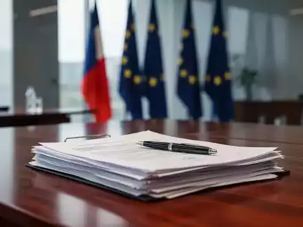 Dokumente auf einem Schreibtisch in einem Regierungsbüro mit EU-Flaggen im Hintergrund als Symbol für rechtliche Änderungen. - Foto: über boerse-global.de