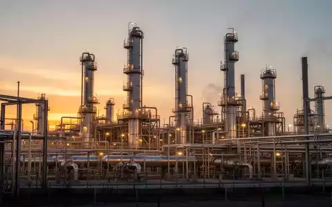 Moderne Ölraffinerie bei Sonnenuntergang mit industriellen Anlagen und atmosphärischer Beleuchtung. - Foto: über boerse-global.de