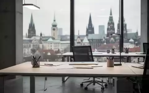 Ein minimalistischer Büroarbeitsplatz vor einer unscharfen Stadtkulisse, symbolisch für die deutsche Wirtschaftslage. - Foto: über boerse-global.de